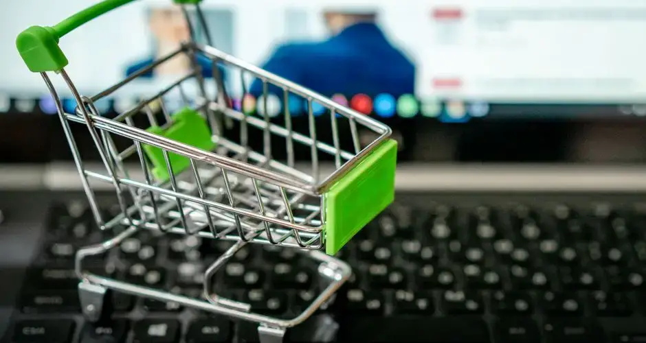 Miniature shopping cart placed on a laptop keyboard, symbolizing online shopping.