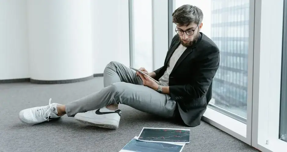 A man in an office setting using a tablet to analyze stock market data with graphs.