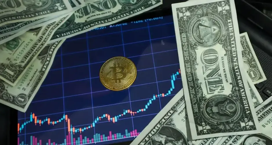 Bitcoin coin on a tablet showing stock chart, surrounded by dollar bills.