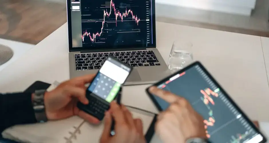Hands using digital devices for financial analysis at a modern desk setup.