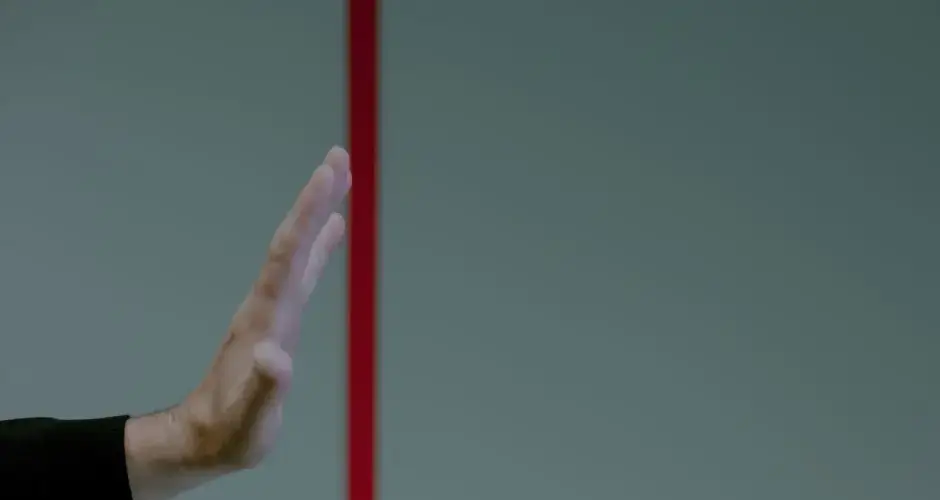 Close-up of a man's hand gesturing stop in front of a vertical red line, concept of boundary.