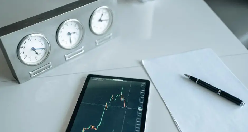 A desk with trading tools, including a tablet showing stock market data and three clocks.