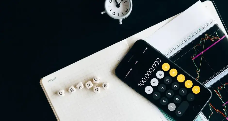 Notebook with an iPhone displaying 100,000,000, desk clock and financial charts suggesting market analysis.