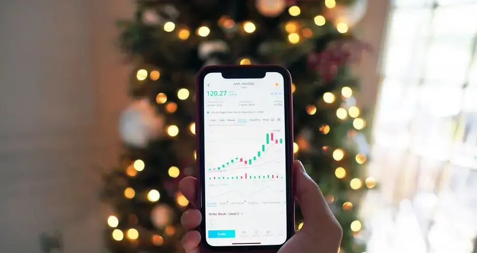 Close-up of a smartphone displaying stock market trading app with a background of Christmas lights.