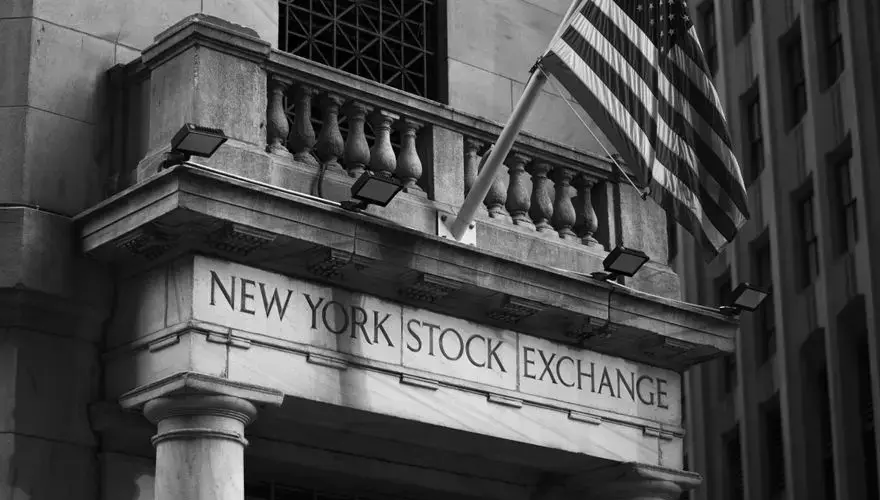 Black and white photo of the New York Stock Exchange facade with USA flag.