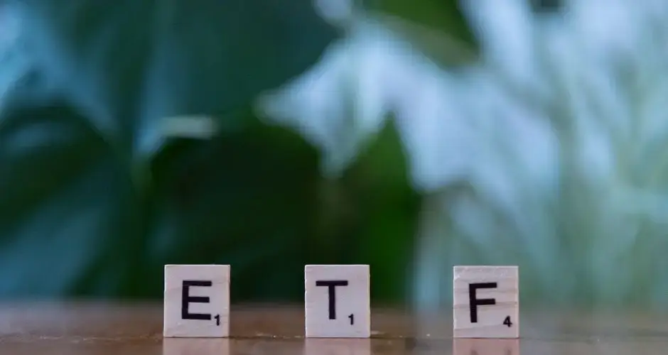 Scrabble tiles spelling ETF on a wooden surface with blurred green background.