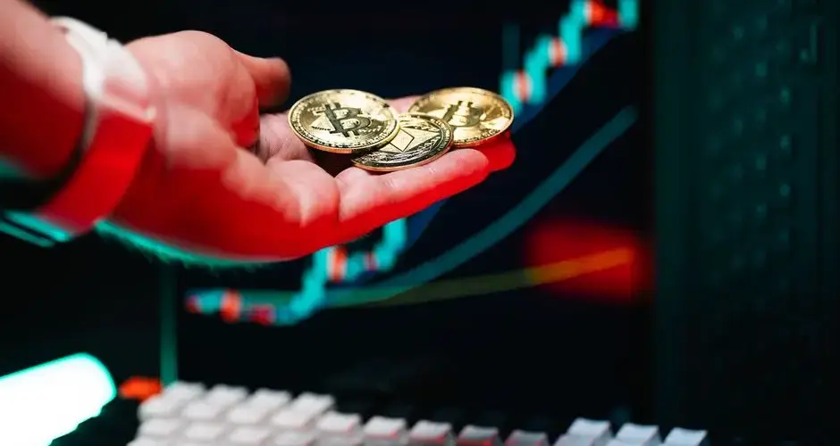 Close-up of hand holding cryptocurrency coins with trading chart in background.