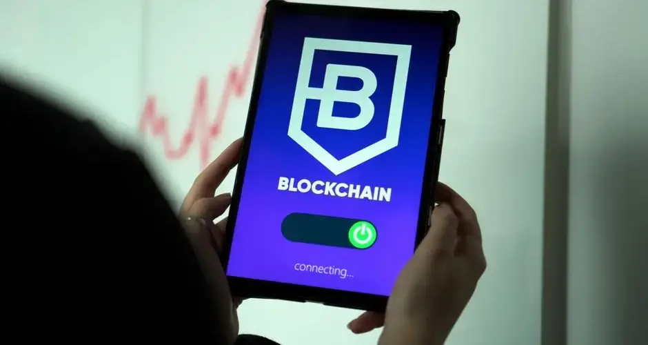 Close-up of hands holding a tablet displaying a blockchain application interface.