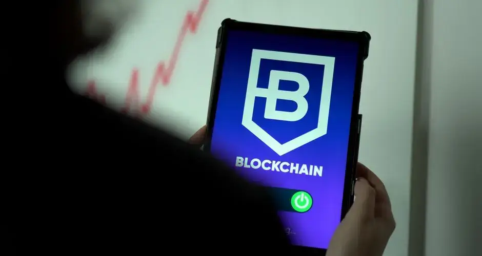 Close-up of hands holding a tablet with blockchain logo on screen, indicating crypto technology.
