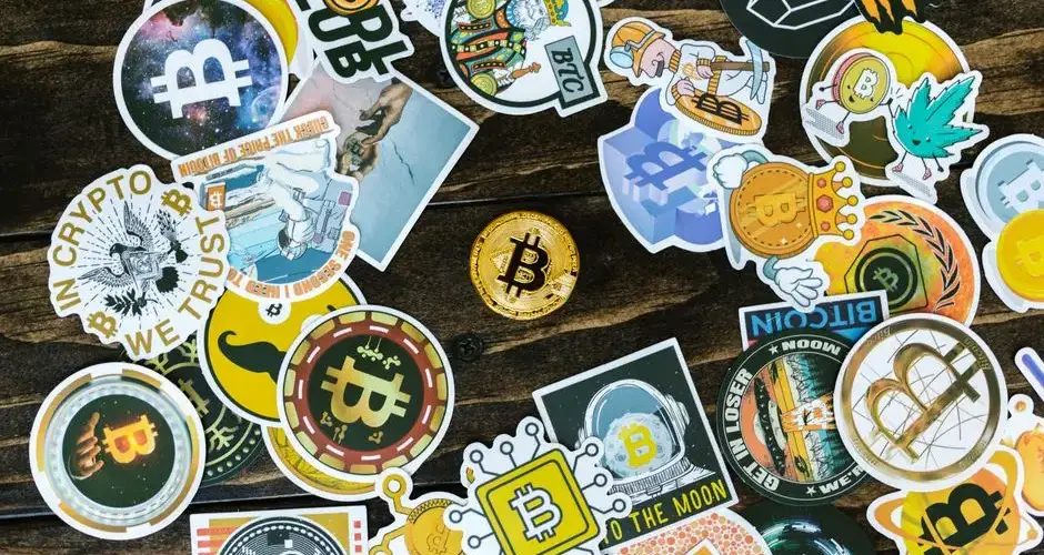 A collection of vibrant Bitcoin-themed stickers and a coin on a wooden surface. Ideal for cryptocurrency concepts.