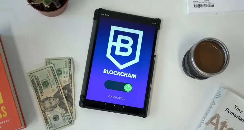 Tablet displaying a blockchain app interface with US dollars, books, and coffee on a white table.