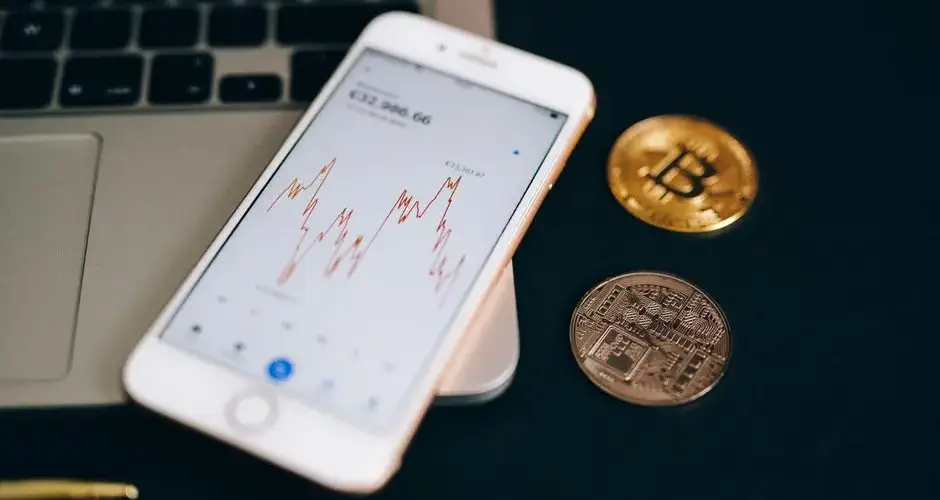 Close-up view of cryptocurrency coins and stock market graph on a smartphone screen.