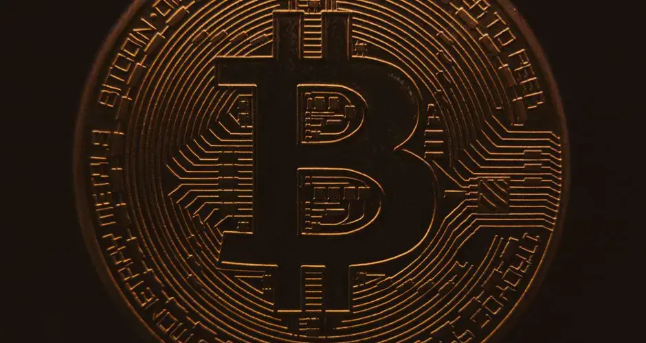 Close-up view of a bitcoin coin showing its intricate, digital design in a warm, dark ambiance.
