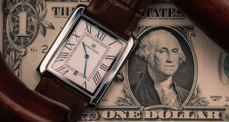 A classic watch placed on a US dollar bill, symbolizing time and money.