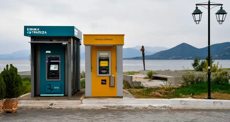 Outdoor ATMs by the Aegean coast in Greece with a scenic view of mountains and sea.