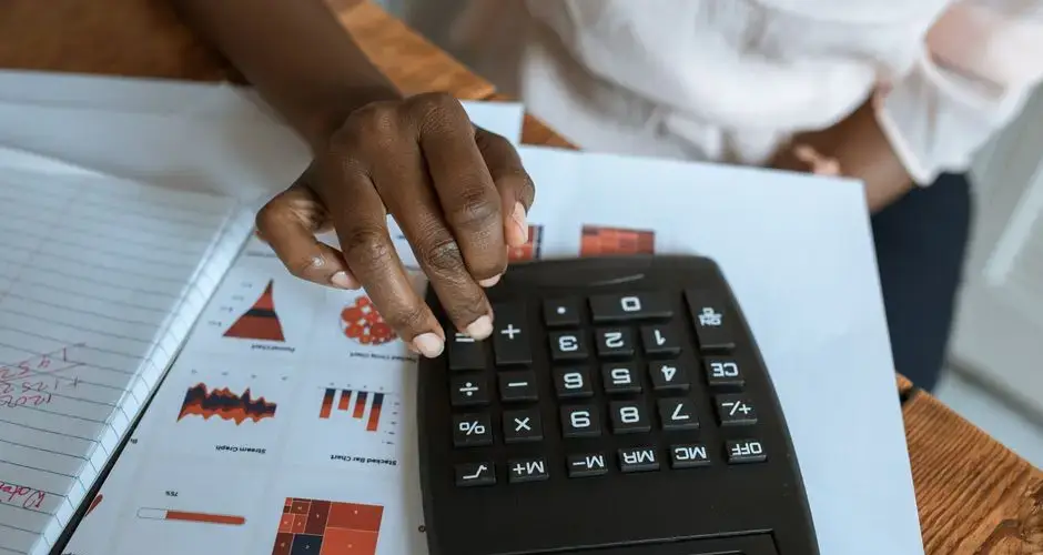 Person using calculator on desk with financial charts and graphs, ideal for business and finance themes.