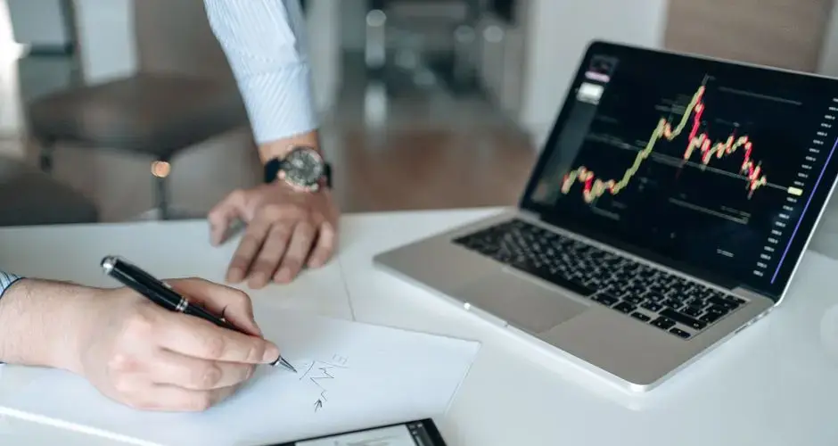 Professional workspace featuring laptop with stock charts, smartphone, and paper for business analysis.