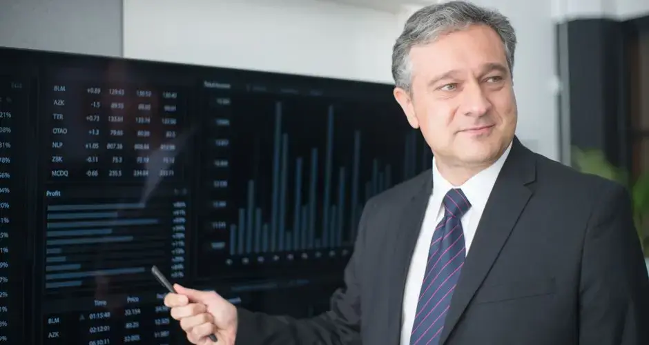 Professional man in suit reviewing financial charts on monitor, showcasing stock market trends.