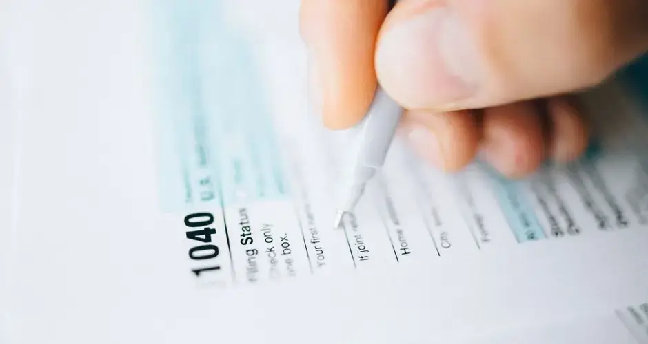 Close-up of a hand using a pen to fill out a tax form 1040, focusing on details.