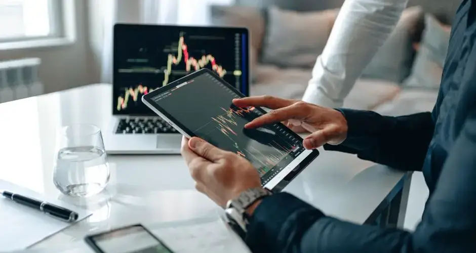 Two professionals using a tablet and laptop to analyze market trends in a modern office setting.