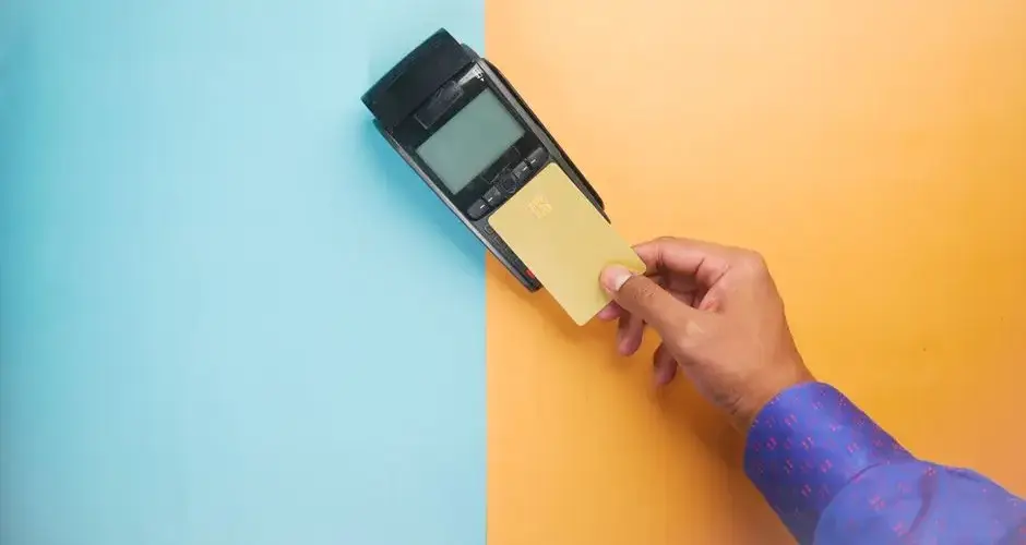 A hand tapping a credit card on a payment terminal for a contactless transaction.