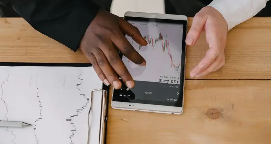 Two professionals analyzing stock market trends on a tablet in an office setting.