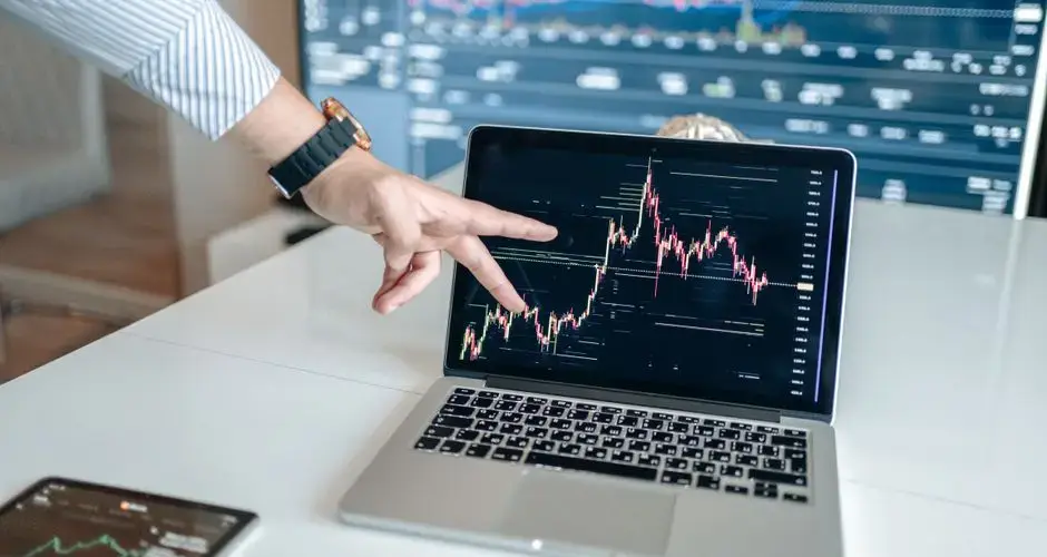 A person pointing at a laptop displaying a cryptocurrency market chart, indicating data analysis.