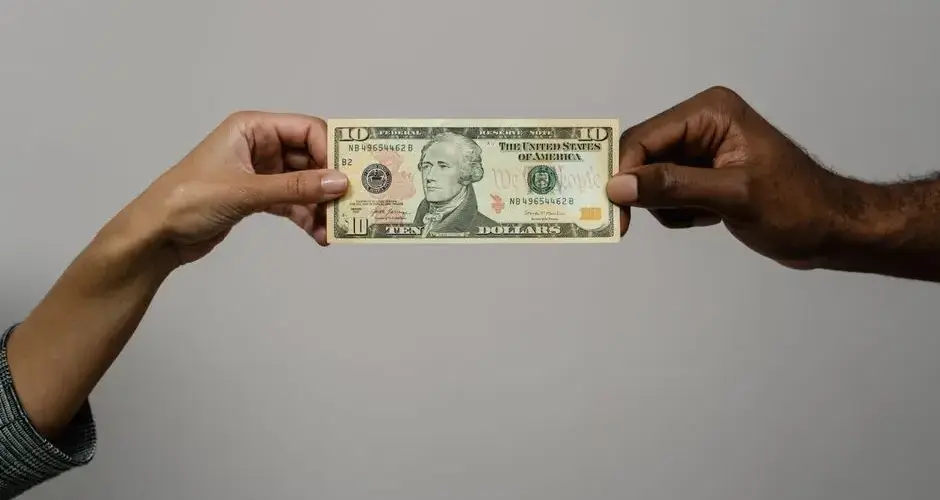 Close-up of two hands exchanging a ten dollar bill, symbolizing financial transaction or exchange.