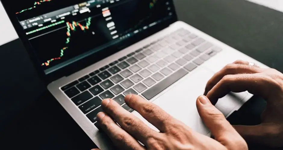 Close-up of hands typing on a laptop with stock market graphs, ideal for finance or business themes.