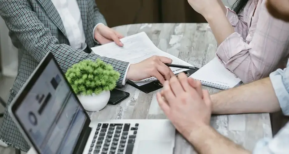 Professional meeting discussing business agreements with laptops and documents on a rustic table.
