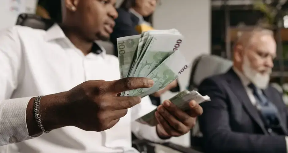 Three professionals in business attire counting cash in a modern office setting.