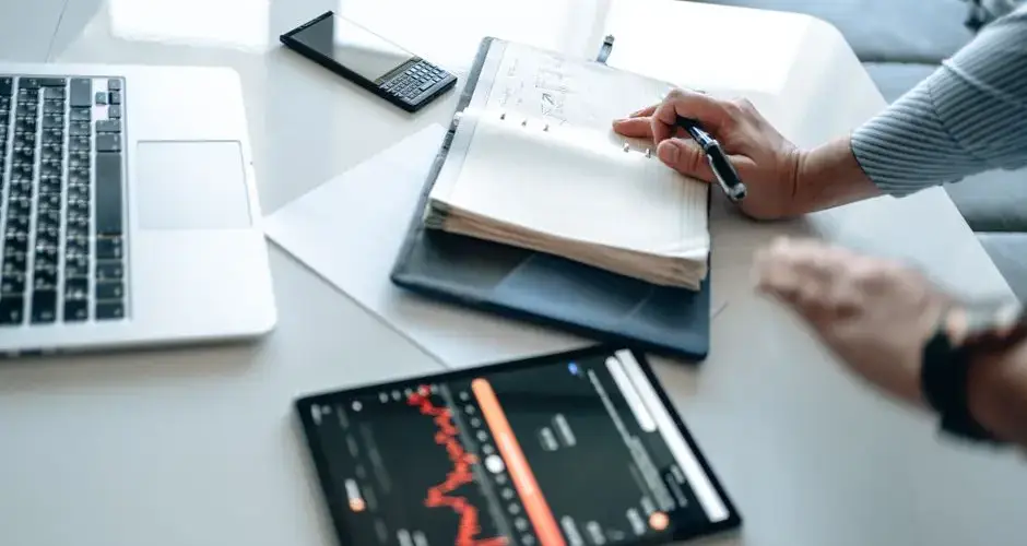 A person analyzing business data using a tablet, laptop, and notebook for efficient work.