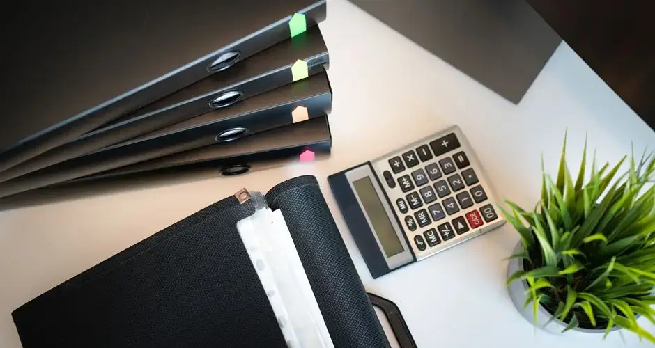 Top view of a tidy office desk with files, a calculator, and a plant, emphasizing organization.