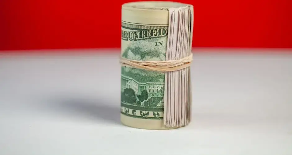 Rolled stack of US dollar bills secured with rubber band on bright surface contrast