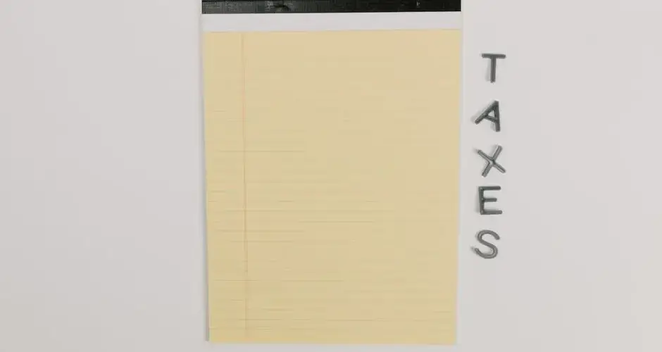 Close-up of a yellow legal pad and the word 'TAXES' on a white surface, ideal for finance themes.