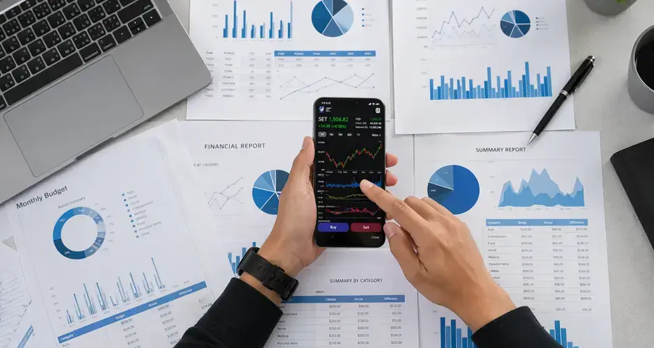 Business person reviews financial data and graphs on a mobile device surrounded by reports.