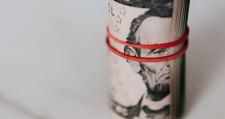 Pack of US five dollar banknotes twisted into roll and tightened with red band