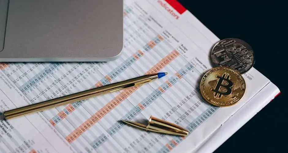 Flat lay of Bitcoin coins on a financial report with a laptop and pen.