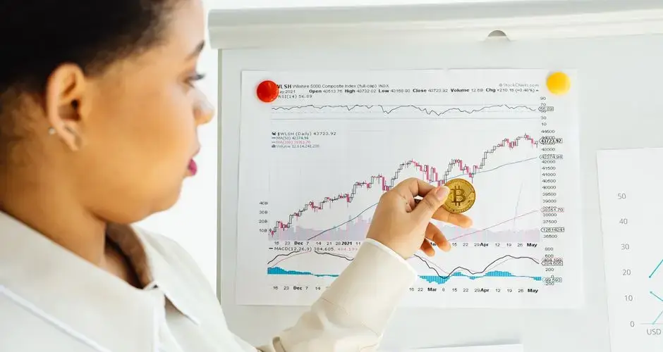 African American woman examines bitcoin and stock market trends on a whiteboard.