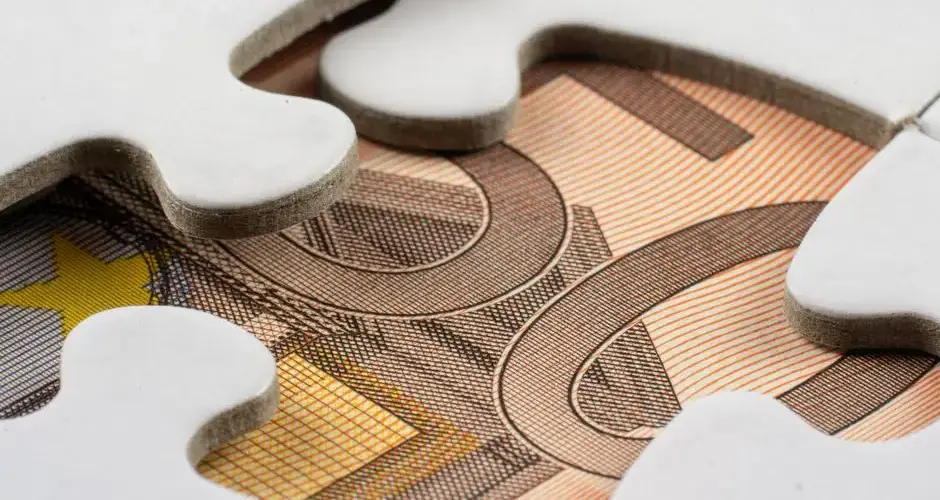 Detailed macro view of white puzzle pieces partially covering a Euro banknote.
