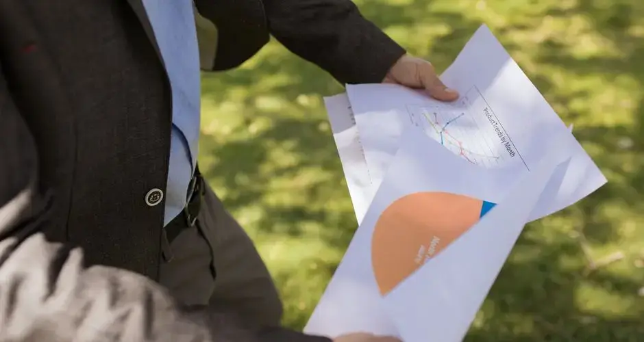 Man in suit holding financial reports in a sunny park.