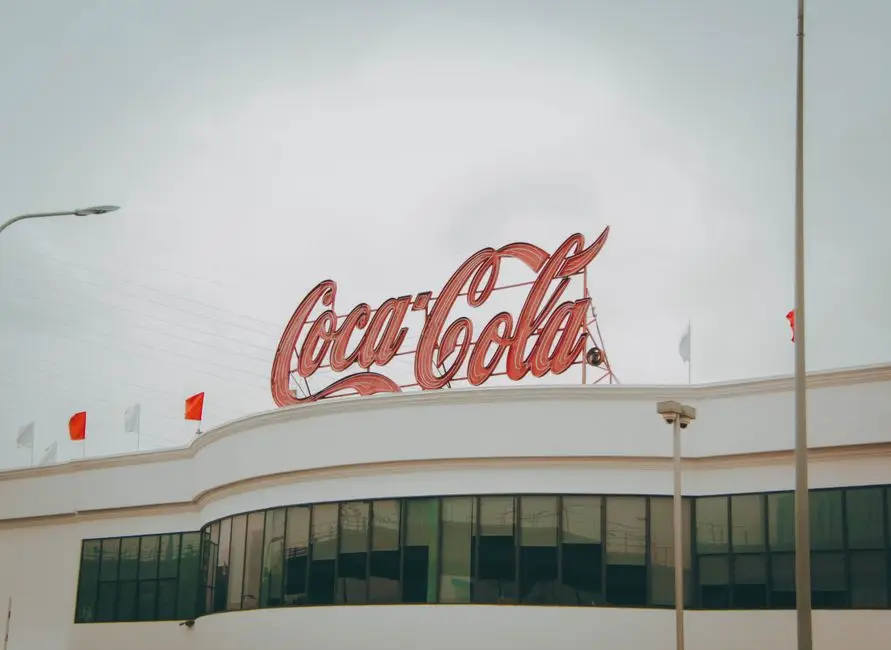 Exterior view of Coca-Cola factory with iconic red sign atop the modern building.