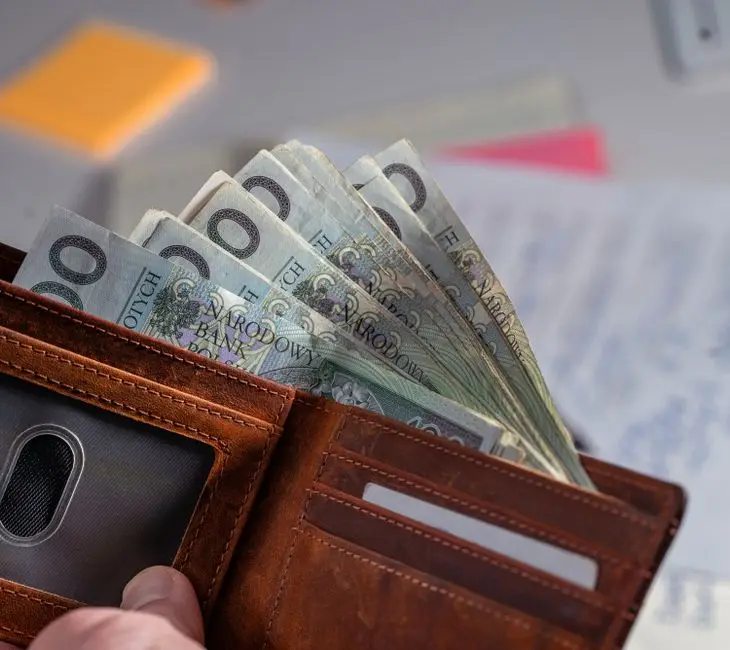 Brown leather wallet containing Polish zloty banknotes on cluttered desk