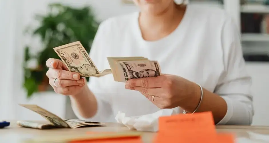 A woman sits indoors counting cash at her office desk, focusing on finances.