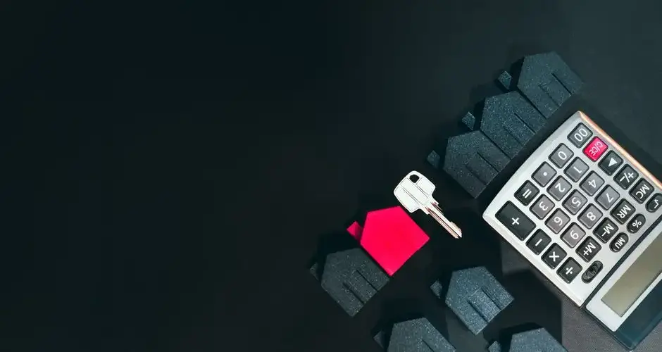 Real estate concept image featuring a calculator, houses, and a key on a black background.