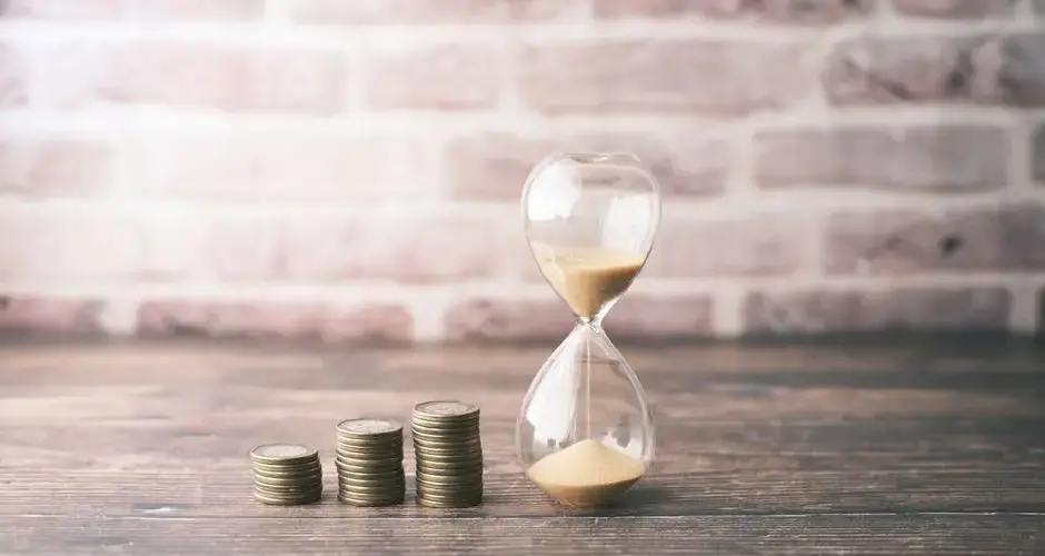 Hourglass and stacked coins on wood, symbolizing the concept of time and money.