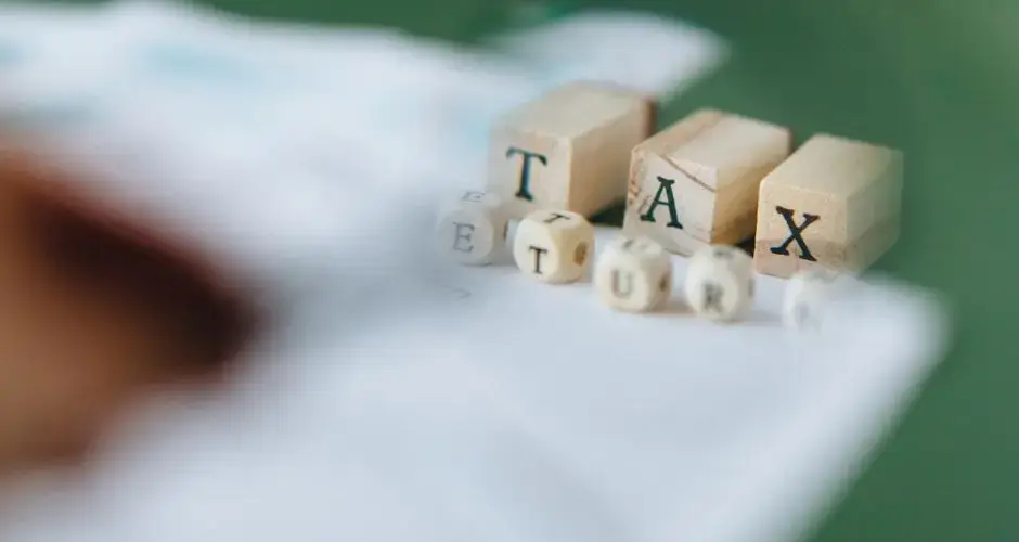 Wooden blocks and dice spelling 'Tax Return' on a blurred green background.
