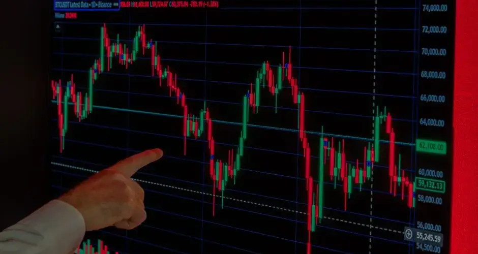 Hand pointing at Bitcoin price graph on screen, highlighting market trends and investment analysis.