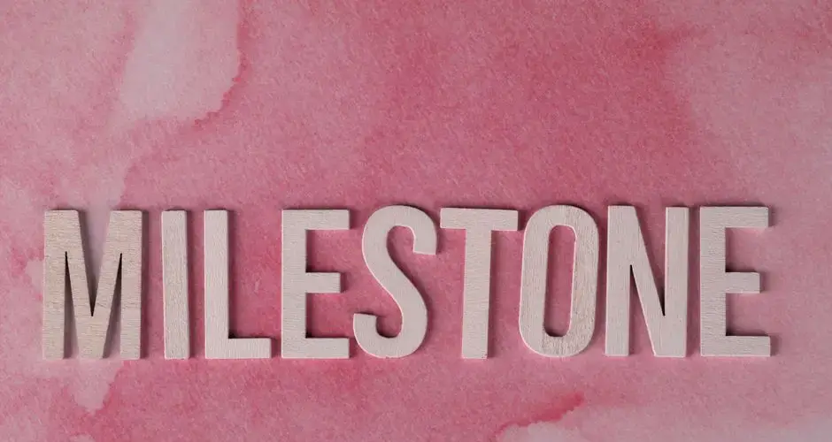 Wooden MILESTONE text on a pink watercolor background, perfect for celebrations or achievements.