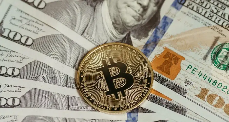A Bitcoin coin placed on a stack of hundred dollar bills, symbolizing cryptocurrency and traditional wealth.